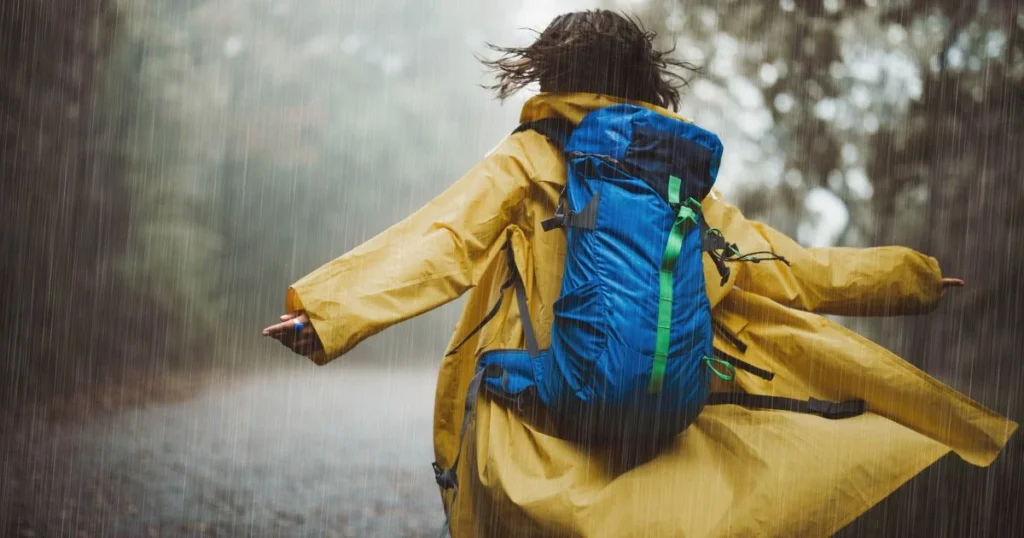 Hiker wearing a blue backpack in heavy rain, showing the importance of keeping hiking gear dry.