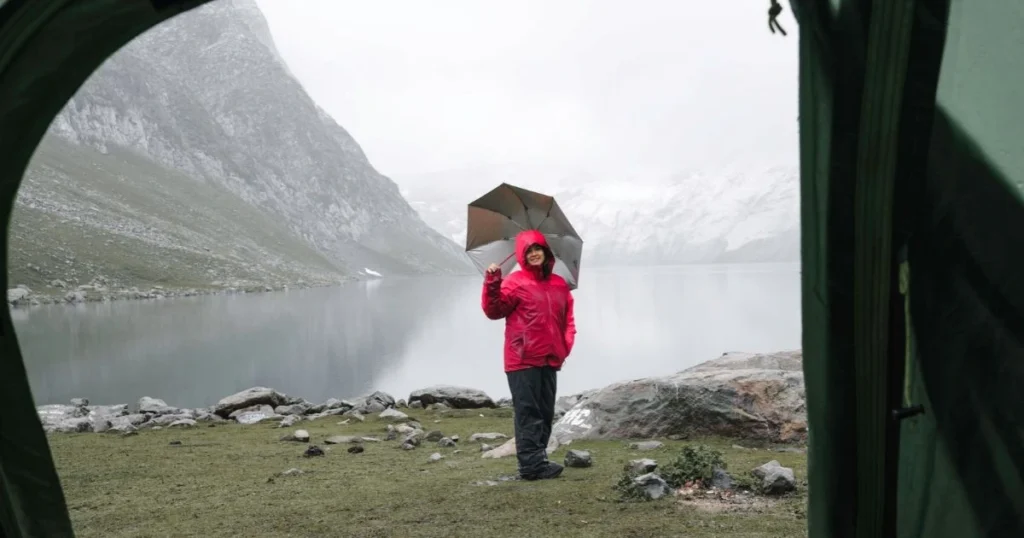 Hiker wearing a red waterproof jacket beside a mountain lake in cold, wet weather.