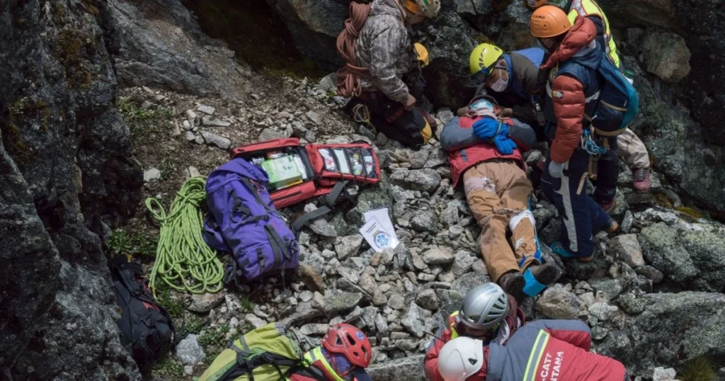 Mountain rescue team assisting an injured hiker on rocky terrain, with first-aid and emergency equipment.
