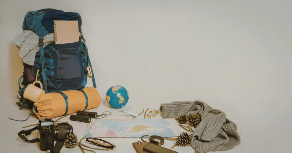 Backpacking gear laid out beside a hiking backpack, including clothing, a map, and outdoor essentials.